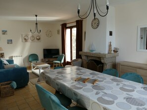 A living room with a dining table, chairs, a television, a fireplace, and a chandelier.
