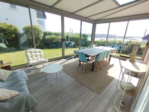 Un patio iluminado por el sol con una mesa de comedor y sillas, una silla con cojín y una pequeña mesa redonda.