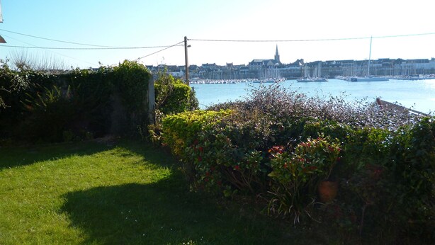 A coastal view with a grassy area, dense shrubbery, and a distant marina with boats. - South Brittany House Sea View in Port-louis 8 -10 people (Port-Louis)