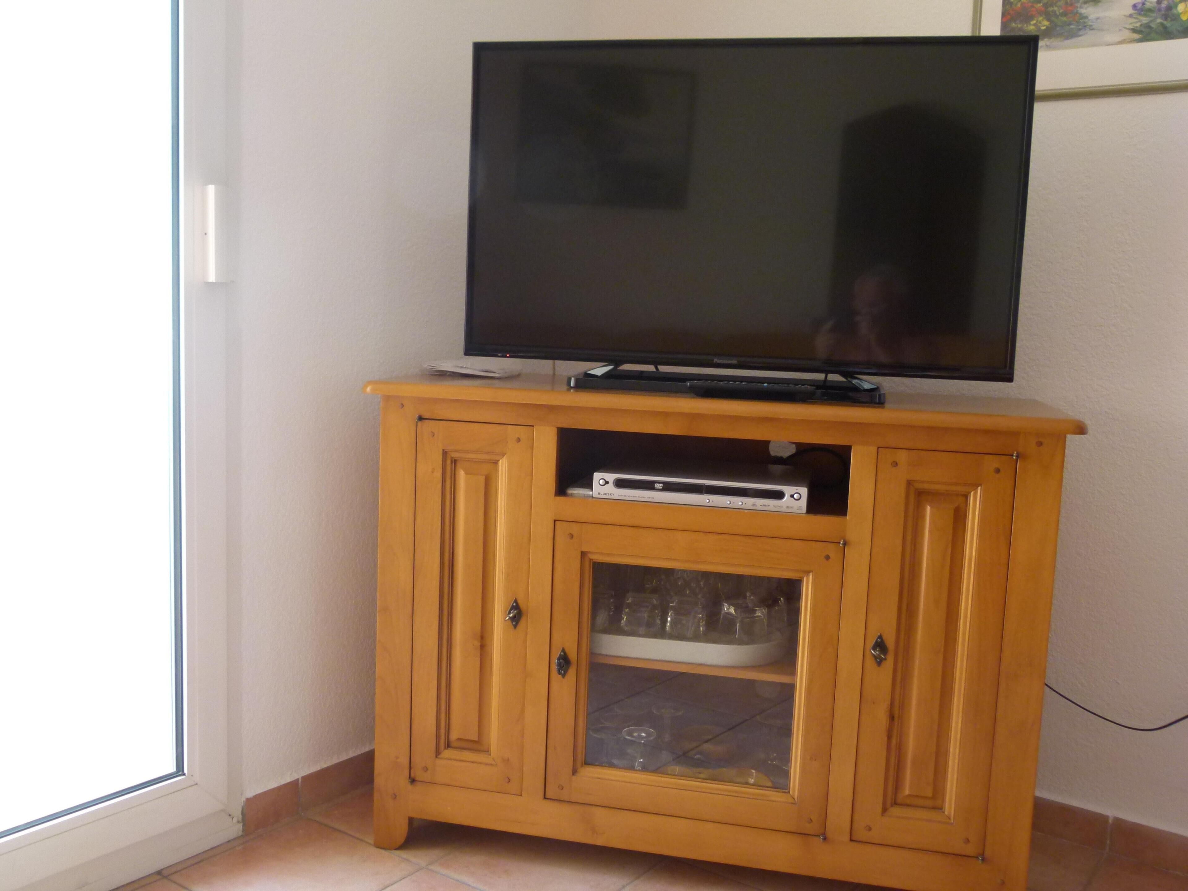 Eine Holzunterhaltungseinheit mit einem Flachbildfernseher, einem DVD-Player und einem gläsernen Schrank mit Geschirr.
