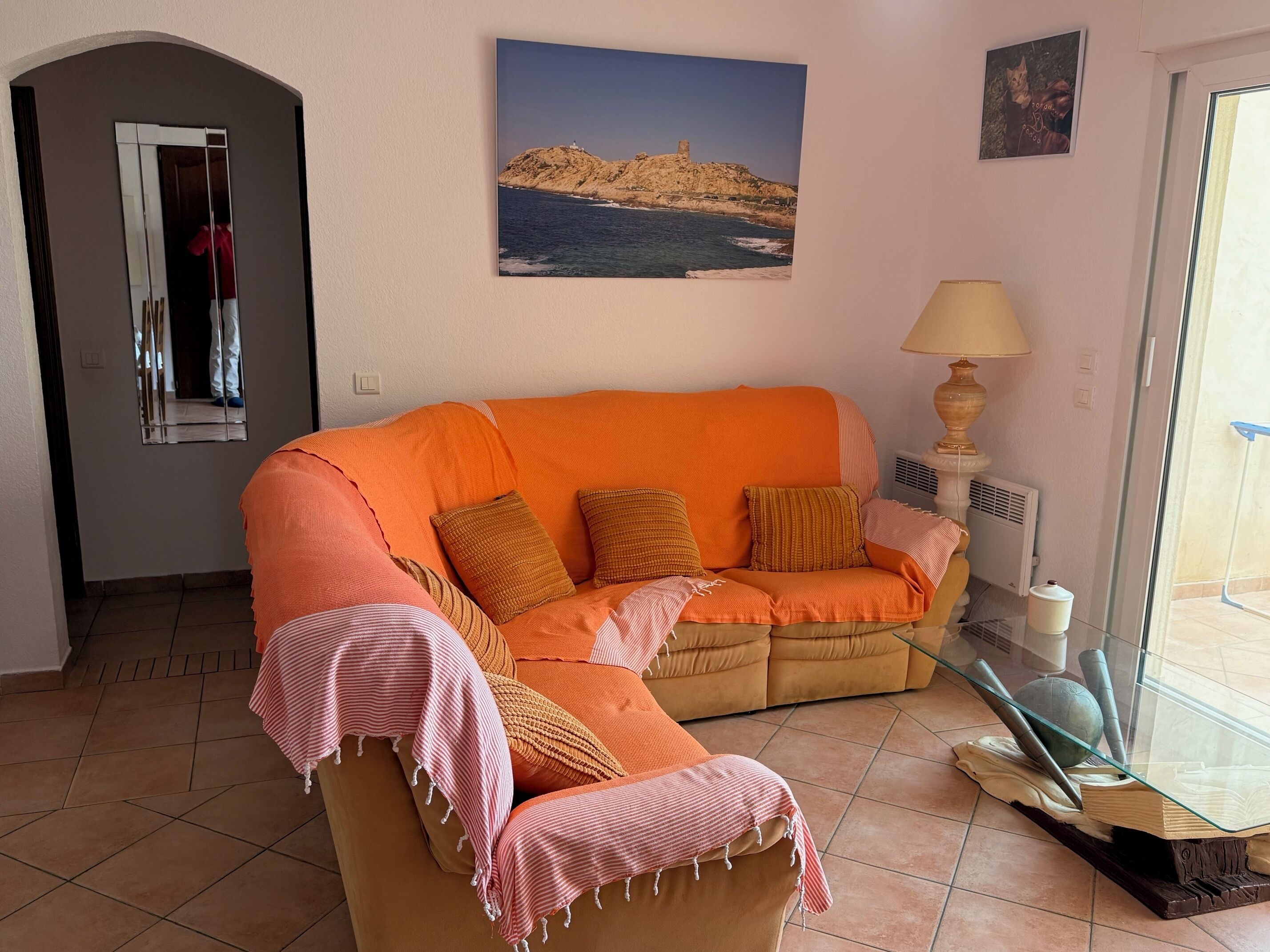 Een woonkamer met een bank, een lamp, een schilderij en een uitzicht door een glazen deur.