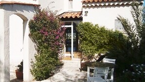 Ein weißes Gebäude mit einem Ziegeldach, einem Steinweg und einer kleinen Terrasse mit Tisch und Stühlen.