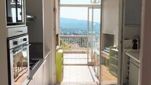Eine moderne Küche mit Backofen, ein Essbereich mit Tisch und ein Balkon mit Blick auf die Stadt.
