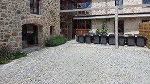 A stone building with a covered patio area, outdoor seating, and a gravel courtyard. - Gîte 25 p, swimming pool, whirlpool, fitness, sauna ⚠️Vérifiez spams⚠️ (Charensat)