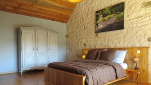 A bedroom with a wooden bed, a stone wall, and a white wardrobe. - Gîte 25 p, swimming pool, whirlpool, fitness, sauna ⚠️Vérifiez spams⚠️ (Charensat)
