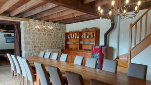 A dining area with a long wooden table, several chairs, a stone wall, a wooden cabinet with glassware, and a staircase. - Gîte 25 p, swimming pool, whirlpool, fitness, sauna ⚠️Vérifiez spams⚠️ (Charensat)