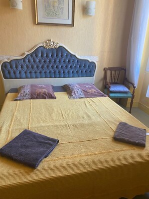 Ein Bett mit einer geblümten Kopfteil, zwei Kissen, einer gelben Tagesdecke und zwei gefalteten Handtüchern.