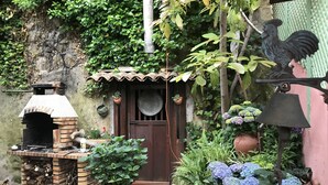 A rustic outdoor kitchen area with a brick oven, potted plants, and a rooster decoration. - VILLA FOR RENT (near the beach with swimming pool, garden barbecue). (Menton)
