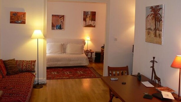 Une pièce confortable avec un lit, une petite table et un canapé. On y trouve des œuvres d’art accrochées au mur et une lampe sur la table.