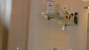 Une salle de bain avec des carreaux blancs, une étagère en verre où sont rangés les articles de toilette, un porte-serviettes et un miroir.