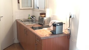 Une petite cuisine avec des meubles de rangement en bois, un évier, une cuisinière et une fenêtre.