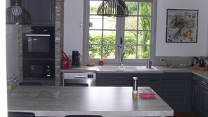 A modern kitchen with a central island, built-in oven, and a large window providing natural light. - Quiet, restful house with private pool in a tourist area (Bout-Du-Pont-De-Larn)