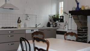 A modern kitchen with white tiles, a stove, a sink, and a dining table with chairs. - Family house near Morlaix, enjoy the countryside and the sea (Plouigneau)