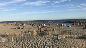 A sandy beach with a wooden fence, people sunbathing and walking, and a clear sky. - 2-3 pers air-conditioned studio with harbor and sea view - Grande Motte (La Grande-Motte)