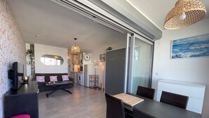 A modern living room with a sofa, coffee table, and dining area. There is a kitchen in the background with appliances and a dining table. - 2-3 pers air-conditioned studio with harbor and sea view - Grande Motte (La Grande-Motte)