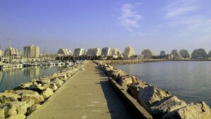 A marina with boats, a concrete walkway, and buildings in the background. - 2-3 pers air-conditioned studio with harbor and sea view - Grande Motte (La Grande-Motte)