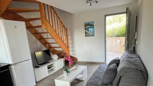 A modern living room with a grey sofa, a white coffee table, a wooden staircase, a white refrigerator, and a laptop on a white cabinet. - T2 apartment, 40 m2, fully air-conditioned, 350 m from the beach. Private parking (Saint Cyr sur Mer)