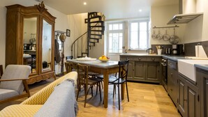 A kitchen with a dining table, chairs, a wooden cabinet, a spiral staircase, and a window. - Le P'tit Pichot Charming Cottage in little wine village 8kms from Beaune (Nantoux)