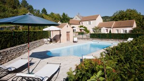 A swimming pool with lounge chairs and umbrellas, surrounded by a stone wall and greenery. - Le P'tit Pichot Charming Cottage in little wine village 8kms from Beaune (Nantoux)