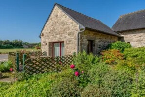 A stone building with a red door, surrounded by greenery and a wooden fence. - Gîte Azalée Romantique 2 persons (Plouarzel)