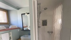 Een badkamer met een douche, een wastafel, een spiegel en een handdoekrek.
