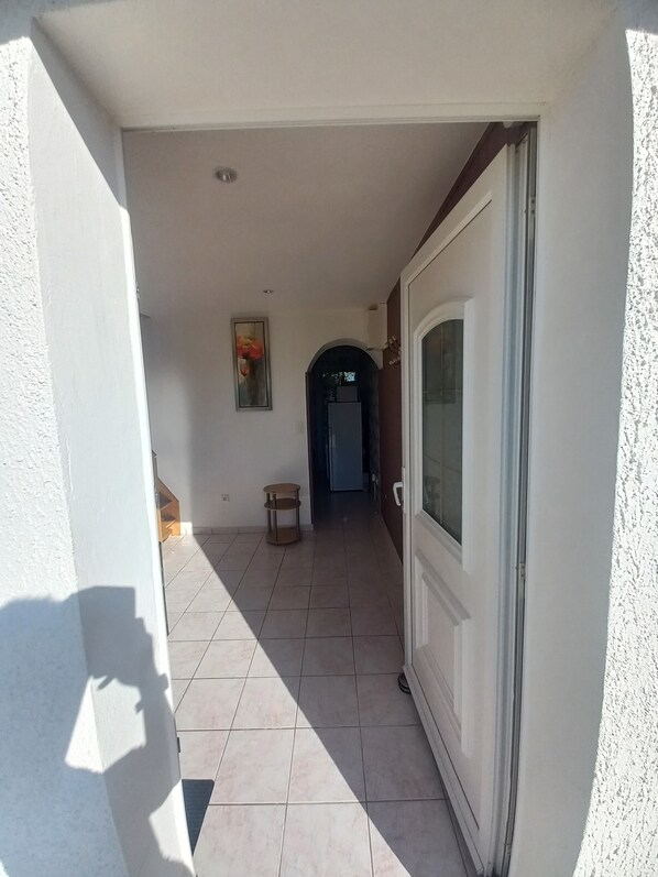 Un pasillo con piso de baldosas que conduce a una puerta con panel de vidrio satinado.