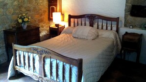 Une chambre à coucher avec un lit en bois, une table de chevet avec une lampe, une commode et un mur en pierre.