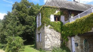 Une maison en pierre aux murs recouverts de lierre, dotée d’un balcon et d’un jardin.