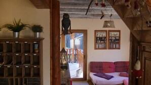 A cozy living room with a wooden bookshelf, a sofa with cushions, and a hanging bird. - Chalet *** surrounded by nature in the heart of Alsace Calm, comfort and authenticity (Fouchy)