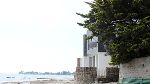 Een strand met een stenen muur, een bankje en een gebouw met een stenen fundering en een balkon.