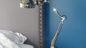 Een nachtkastje met een lamp, een bed met een gestreept kussen en een blauwe muur.