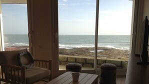 Een kamer met uitzicht op de oceaan, een houten tafel, een stoel en een raam met uitzicht op het strand.