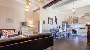 A modern living room with a sofa, a dining area with a table and chairs, and a kitchen with appliances and wooden cabinets.