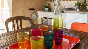 A dining table with a tray holding colorful glasses and a bottle, set against a rustic interior with stone walls and a wooden ceiling.