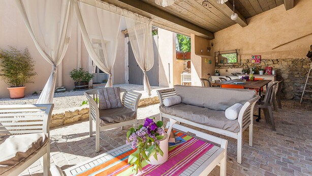 An outdoor patio with white furniture, a colorful rug, and a potted plant.