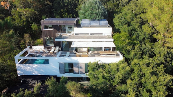 A modern multi-story house with a rooftop pool, large windows, and a deck area.