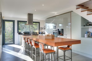 A modern kitchen with a long wooden island, bar stools, and a view of the outdoors.