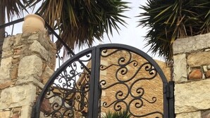 A wrought iron gate with intricate scrollwork, set against a stone wall with a small window. - House located in the center of an exceptional region to discover ! (Platanias Pirgos Spilorenou Crète)