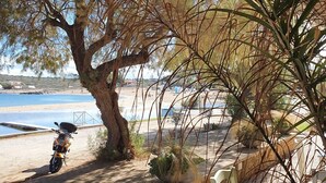 A beachside seating area with a motorcycle parked under a tree, overlooking the sea. - House located in the center of an exceptional region to discover ! (Platanias Pirgos Spilorenou Crète)