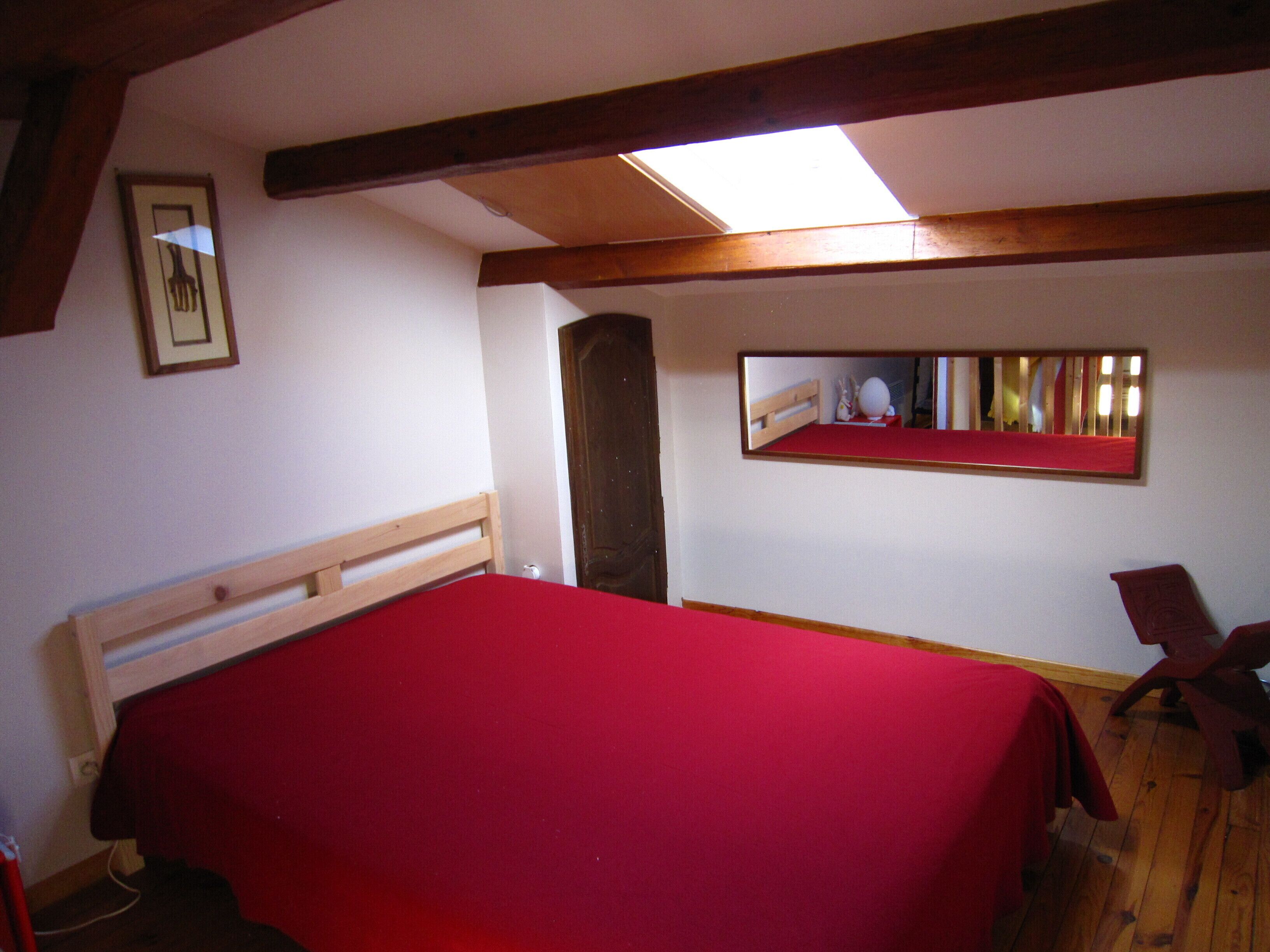 A bedroom with a bed, a wooden headboard, a skylight, a mirror, and a chair.