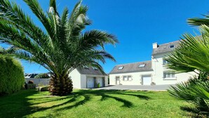 A two-story house with a white exterior, a garage, and a well-maintained lawn with a palm tree.
