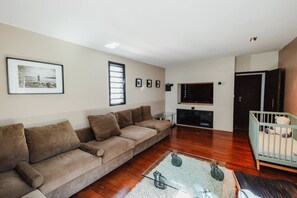 A living room with a sofa, a TV, a crib, and a framed picture on the wall.