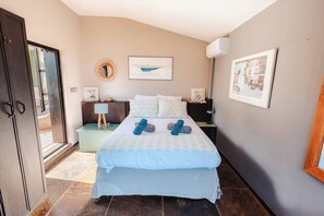 A bedroom with a bed, a nightstand, a wall-mounted air conditioner, and a door leading to a balcony.