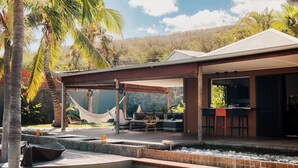 A covered outdoor area with seating, a pool, and a view of a mountainous landscape.