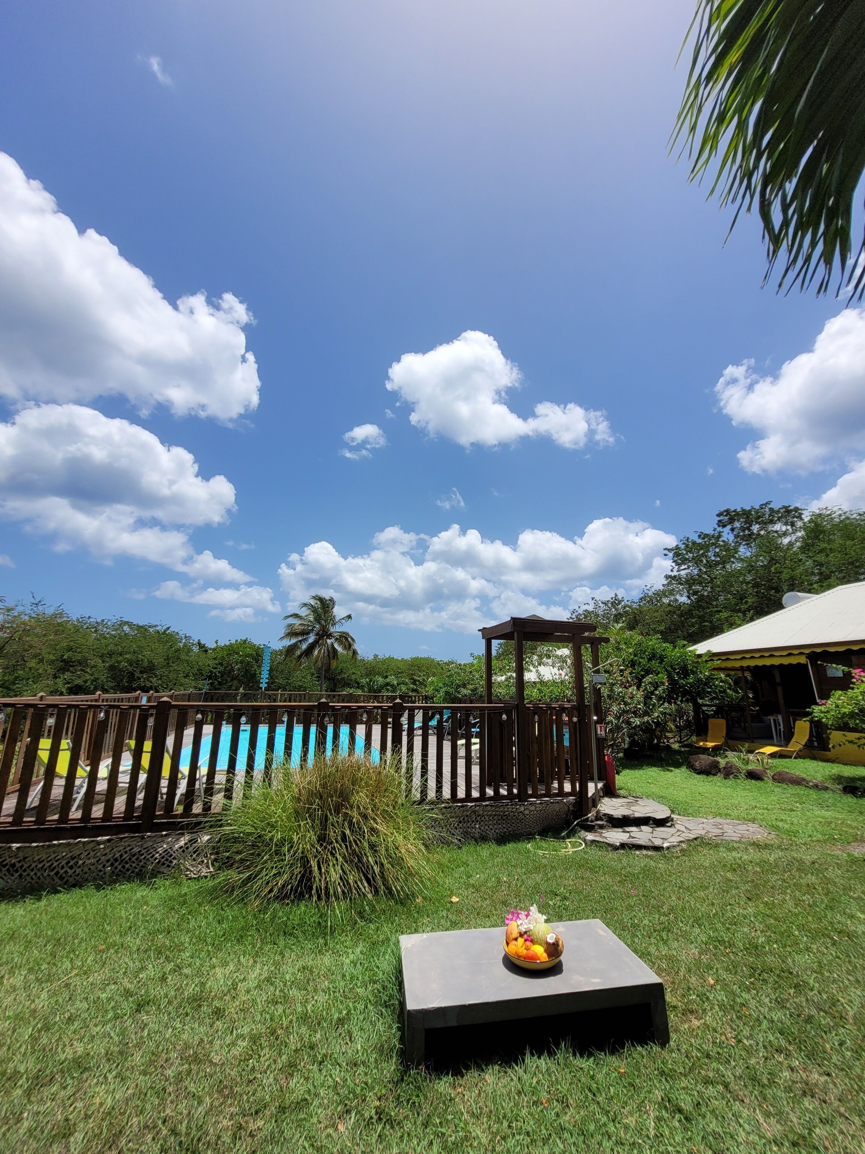 A pool area with a wooden fence, a gazebo, and a table with a fruit bowl.
