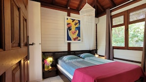 A bedroom with a wooden ceiling, a bed with a red blanket, a painting on the wall, and a window with curtains. - BUNGALOWS "Coco" typical Creole with all comforts, feet in the water  (DESHAIES)