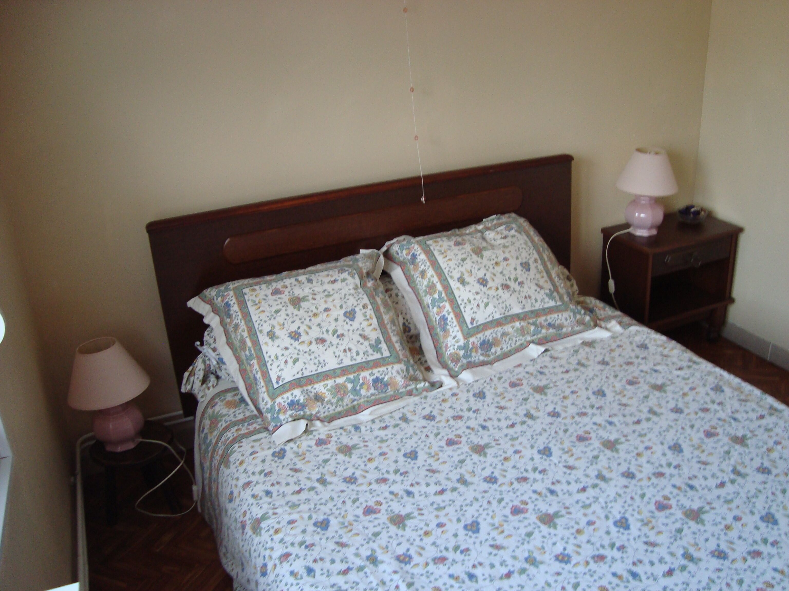 A bedroom with a wooden headboard, floral bedding, two bedside lamps, and a nightstand with a lamp.