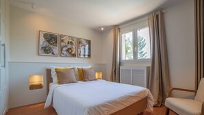 A bedroom with a bed, bedside lamps, a chair, a window with curtains, and wall art.