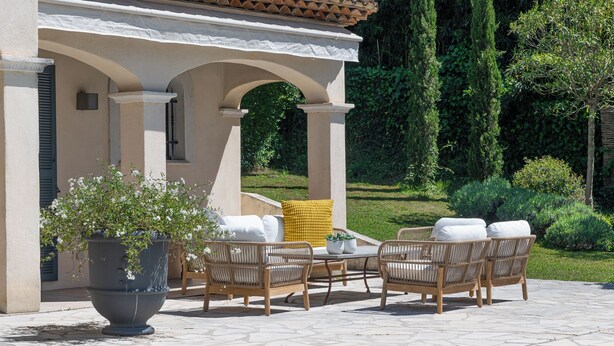 A patio with wicker furniture, a large planter, and a pool.