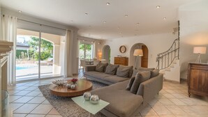 A spacious living room with a large sofa, a coffee table, and a view of a pool and garden through large sliding glass doors.